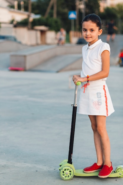 Vista lateral de la niña sonriente de pie en verde scooter