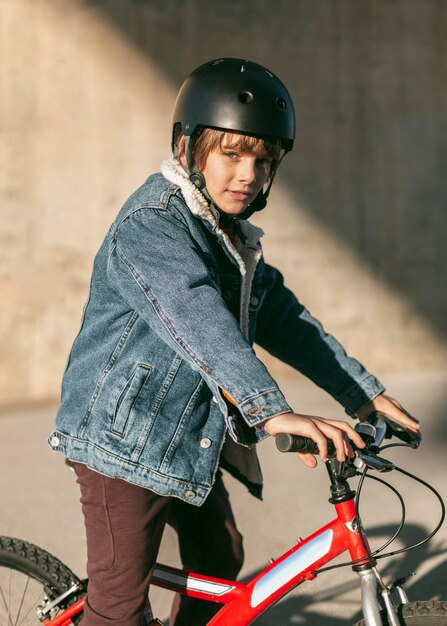 Vista lateral del niño con casco de seguridad posando en su bicicleta