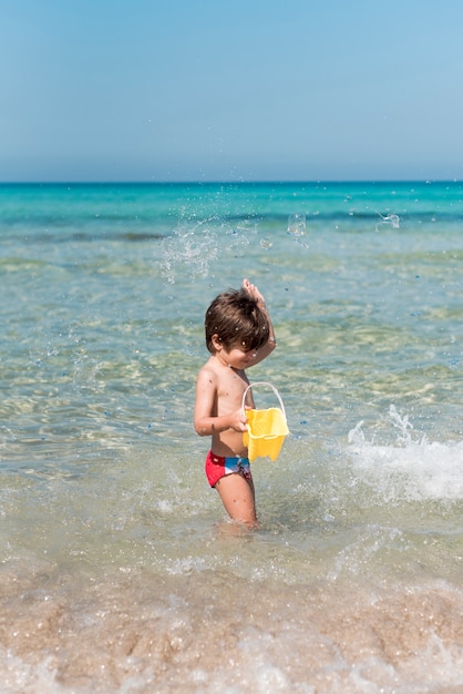 Vista lateral de un niño jugando con un balde en el agua en la playa