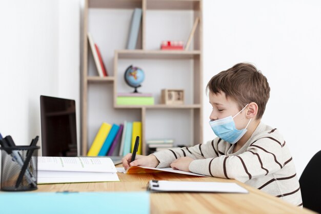 Vista lateral del niño con máscara médica y haciendo la tarea