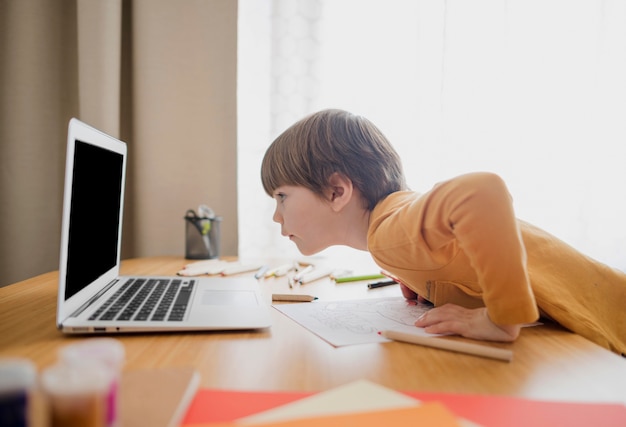 Vista lateral del niño mirando portátil mientras aprende desde casa