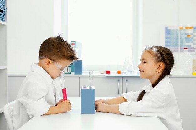 Vista lateral del niño y la niña científicos en el laboratorio con gafas de seguridad