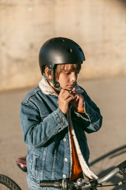 Vista lateral del niño poniéndose el casco de seguridad antes de montar en bicicleta