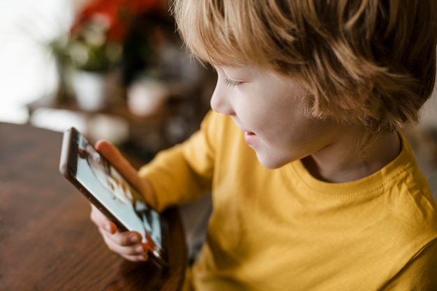 Vista lateral del niño sonriente con smartphone en casa