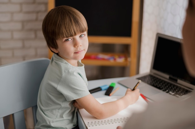 Foto gratuita vista lateral del niño tutorizado en casa con notebook y laptop