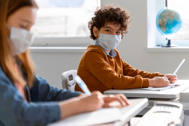 Vista lateral de niños con máscaras médicas en el aula de aprendizaje