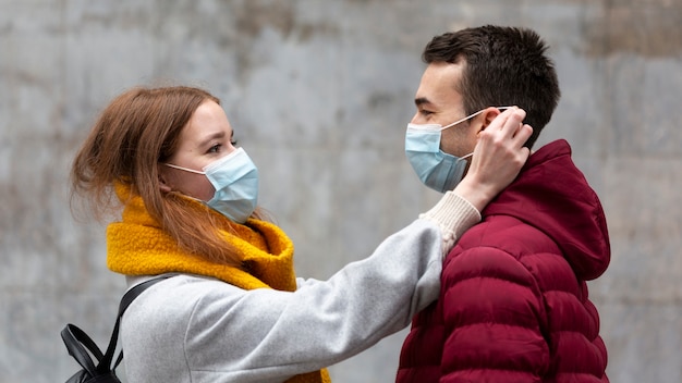 Foto gratuita vista lateral de la novia arreglando la máscara médica del novio