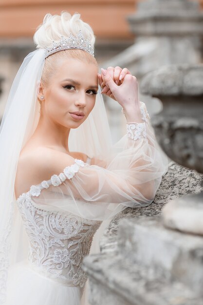 Vista lateral de la novia con estilo en un elegante vestido blanco en la calle mirando a la cámara