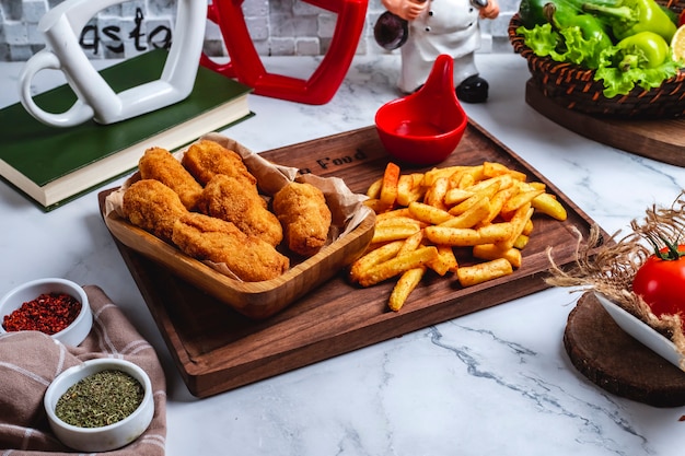 Vista lateral nuggets de pollo con papas fritas y salsa de tomate en el tablero