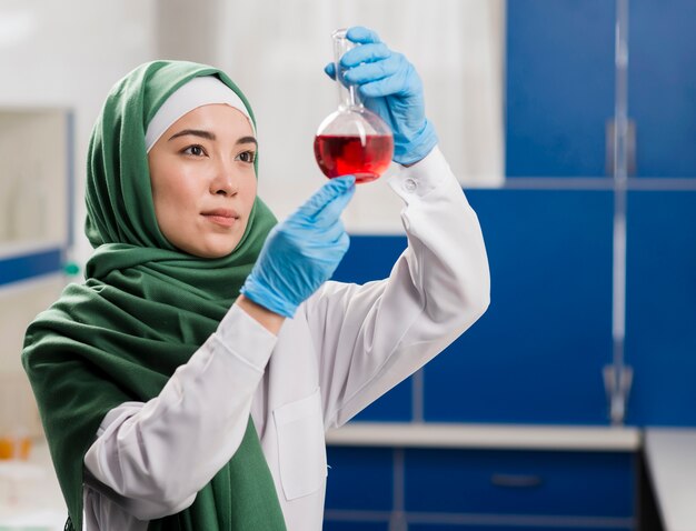 Vista lateral o mujer científico con hijab en el laboratorio mirando sustancia