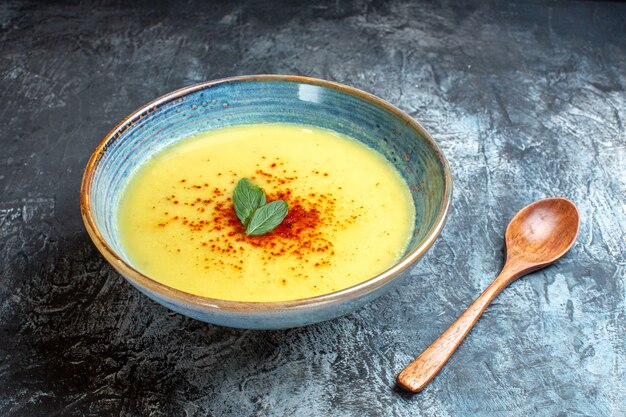 Vista lateral de una olla azul con sabrosa sopa servida con menta y cuchara de madera en la mesa azul