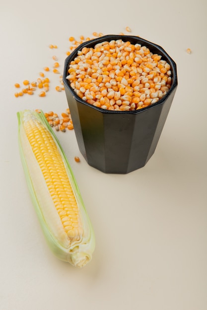 Vista lateral de la olla llena de semillas de maíz y maíz en la mesa blanca