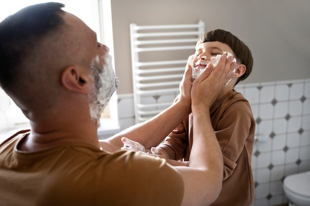 Vista lateral padre poniendo crema de afeitar en la cara del niño