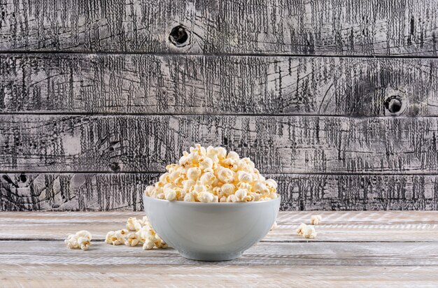 Vista lateral de palomitas de maíz en un tazón en la mesa de madera blanca horizontal