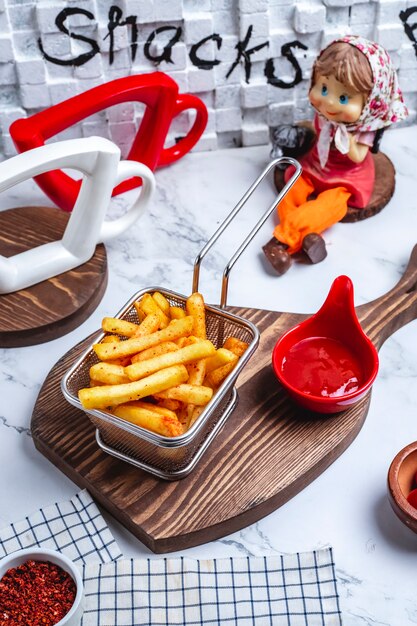 Vista lateral de papas fritas en una canasta con salsa de tomate en el tablero