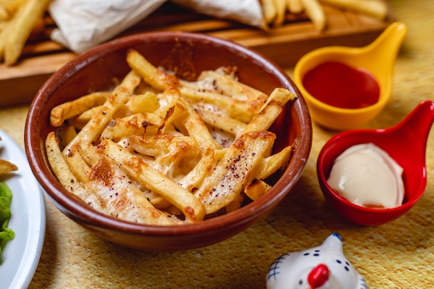 Vista lateral papas fritas con mayonesa de queso derretido y salsa de tomate sobre la mesa