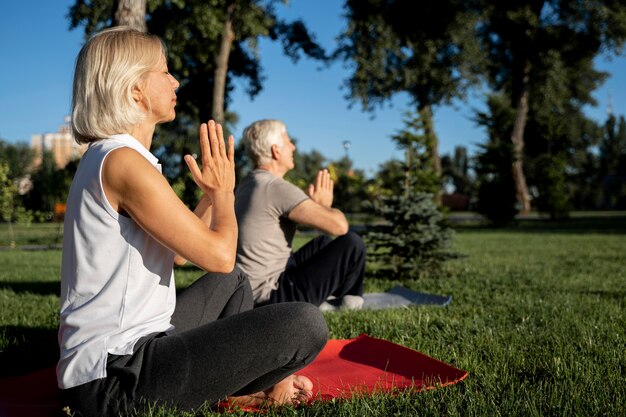 Vista lateral de la pareja de ancianos practicando yoga al aire libre con espacio de copia