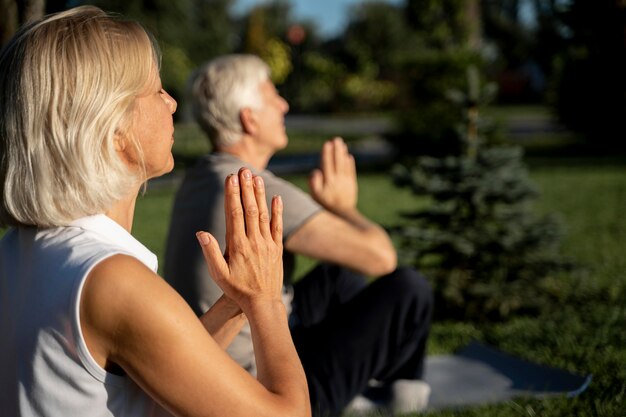 Vista lateral de la pareja de ancianos practicando yoga al aire libre