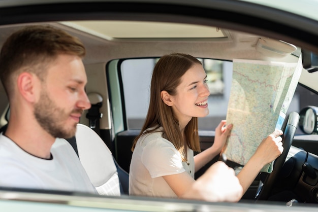 Vista lateral de la pareja en el auto mirando el mapa