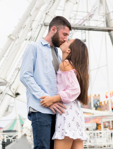 Vista lateral de la pareja besándose en el parque de atracciones