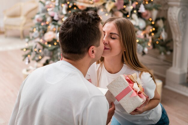 Vista lateral de la pareja besándose con regalos delante del árbol de navidad