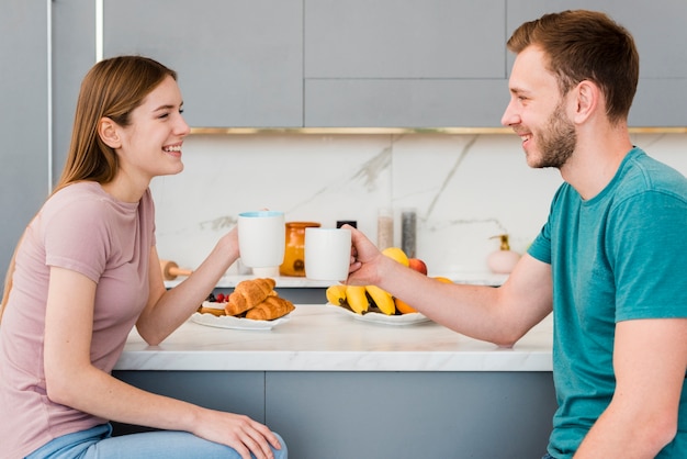 Vista lateral de la pareja en la cocina con tazas