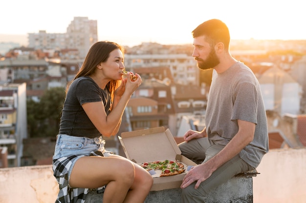 Foto gratuita vista lateral de la pareja comiendo pizza al aire libre