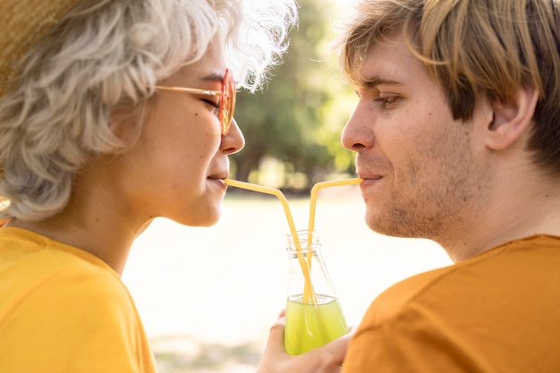 Vista lateral de la pareja compartiendo una botella de jugo en el parque