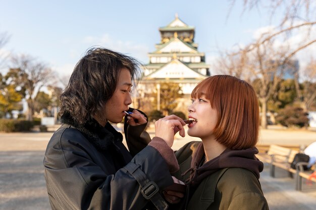 Vista lateral de una pareja japonesa alimentándose mutuamente con dulces de chocolate al aire libre