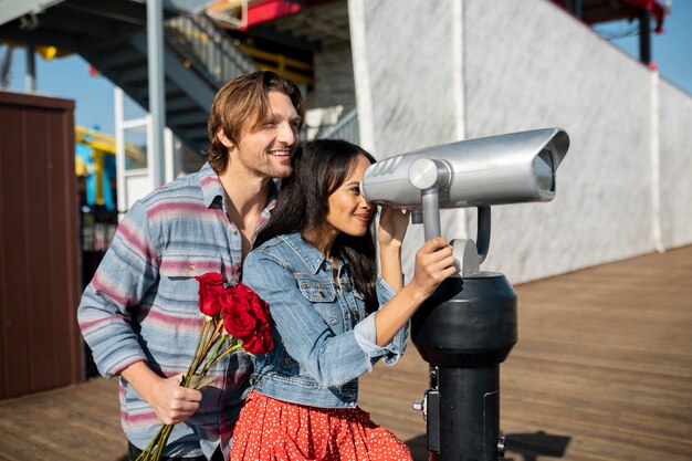 Vista lateral de una pareja joven en una cita al aire libre mirando a través del telescopio