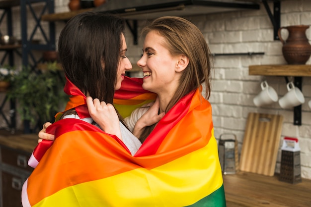 Foto gratuita vista lateral de una pareja joven lesbiana romántica envuelta en una bandera lbgt