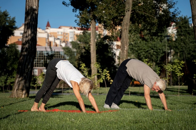 Foto gratuita vista lateral de la pareja madura practicando yoga al aire libre