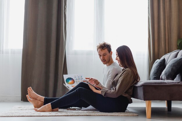 Vista lateral de la pareja que planea redecorar la casa mientras está sentada en el suelo