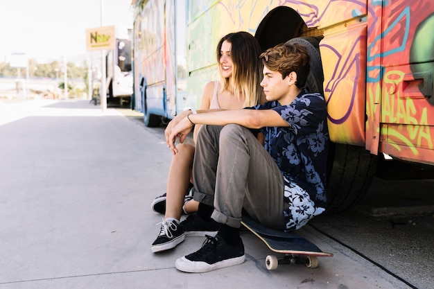 Vista lateral de pareja skater apoyada contra un autobús