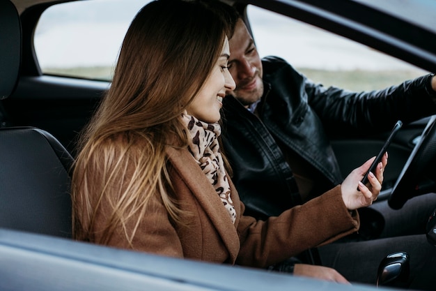 Vista lateral de la pareja con smartphone en el coche