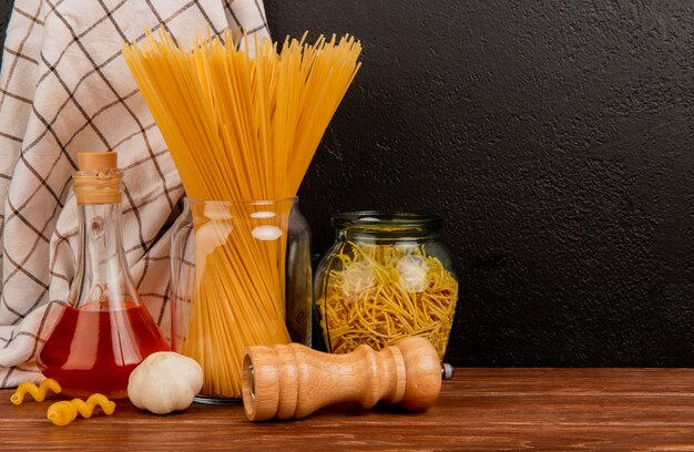 Vista lateral de pasta de espagueti en frascos con mantequilla derretida, ajo, sal y tela escocesa sobre superficie de madera y fondo negro con espacio de copia