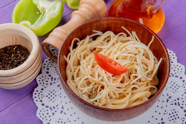 Vista lateral de pasta de espagueti en un tazón sobre tapete de papel con sal de mantequilla de pimienta a medio cortar y pimienta negra sobre superficie morada