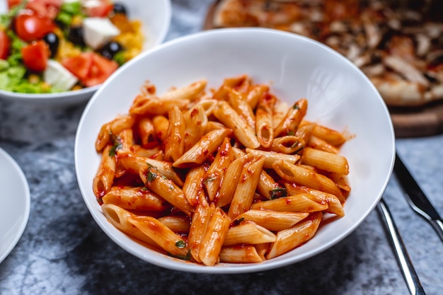 Vista lateral de pasta penne con salsa de tomate, sal, pimienta y hierbas en un plato