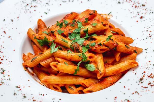 Vista lateral de pasta penne con salsa de tomate y verduras en un plato