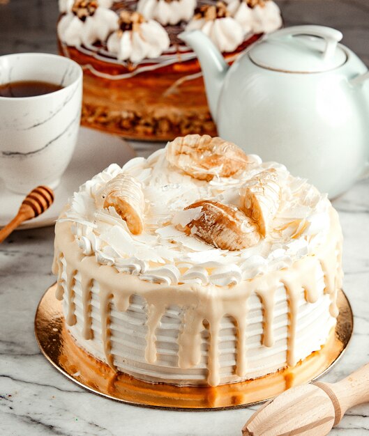 Vista lateral del pastel blanco decorado con crema batida de chocolate blanco derretido y plátanos sobre la mesa