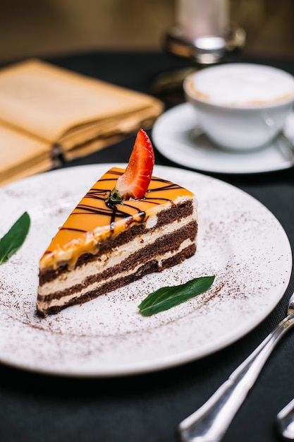Vista lateral del pastel de chocolate en capas cubierto con caramelo una rebanada de fresa en un plato blanco