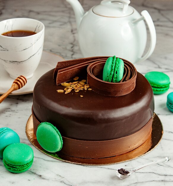 Vista lateral del pastel de chocolate decorado con macarrones verdes servido con té sobre la mesa
