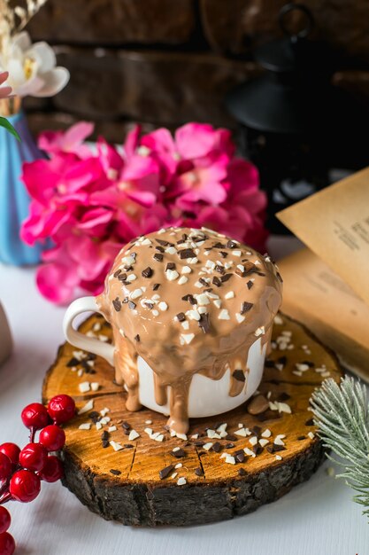 Vista lateral del pastel de chocolate con leche con chispitas de chocolate en una taza sobre una tabla de madera