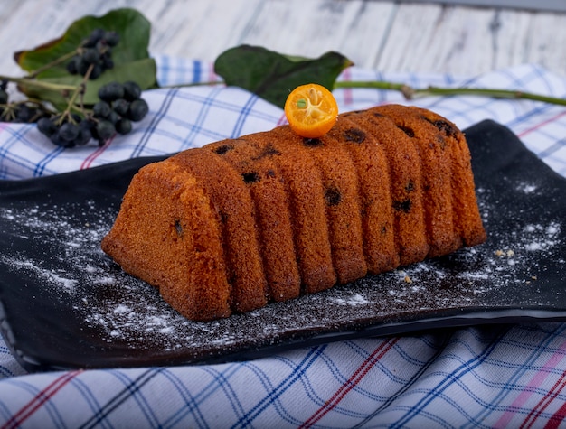 Foto gratuita vista lateral del pastel con pasas decoradas con una rodaja de kumquat y azúcar en polvo sobre una pizarra negra