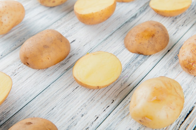 Foto gratuita vista lateral del patrón de papas enteras y cortadas sobre fondo de madera con espacio de copia