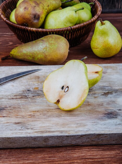 Vista lateral de peras maduras frescas y mitades en una tabla de cortar de madera con cuchillo de cocina sobre fondo rústico