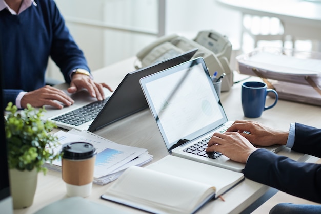 Vista lateral de personas de negocios recortadas irreconocibles que trabajan en un escritorio común