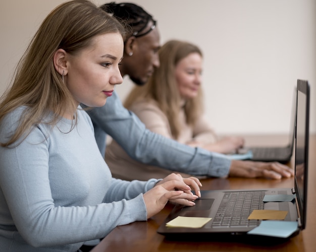 Vista lateral de las personas que trabajan en la computadora portátil en la oficina