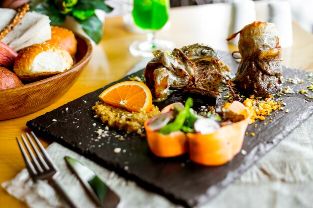 Vista lateral de pescado frito con salsa y una rodaja de naranja con verduras