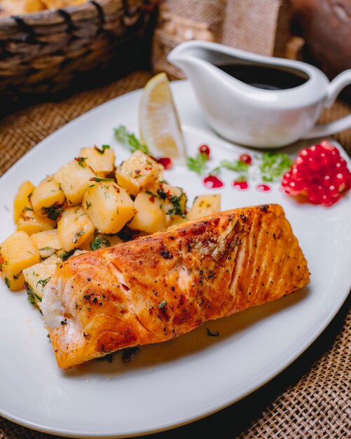 Vista lateral pescado rojo frito con papas y una rodaja de limón con salsa de granada